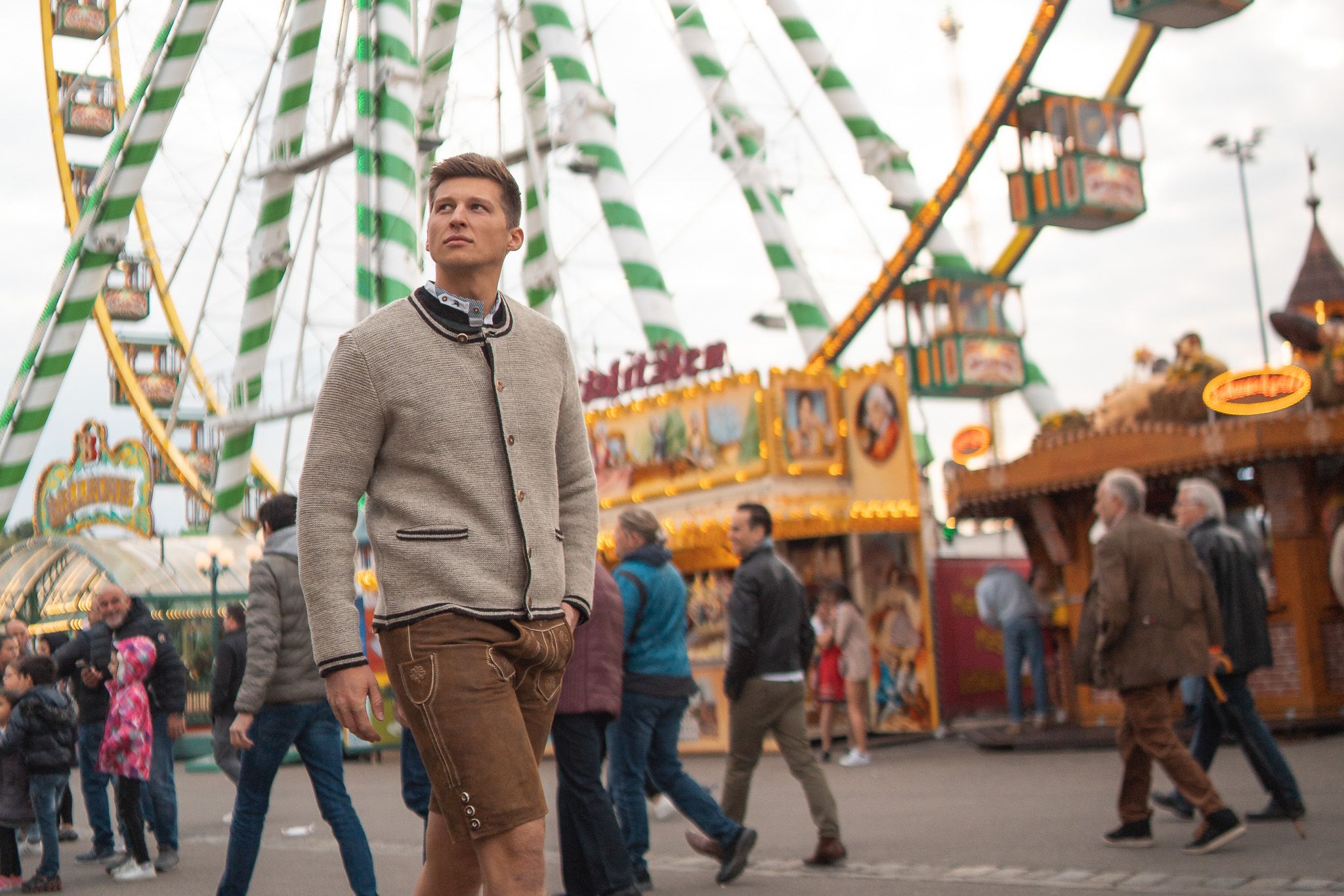 Mann in Lederhose und Trachtenstrickjacke läuft übers Frühlingsfest in Stuttgart. Im Hintergrund ist ein Riesenrad.